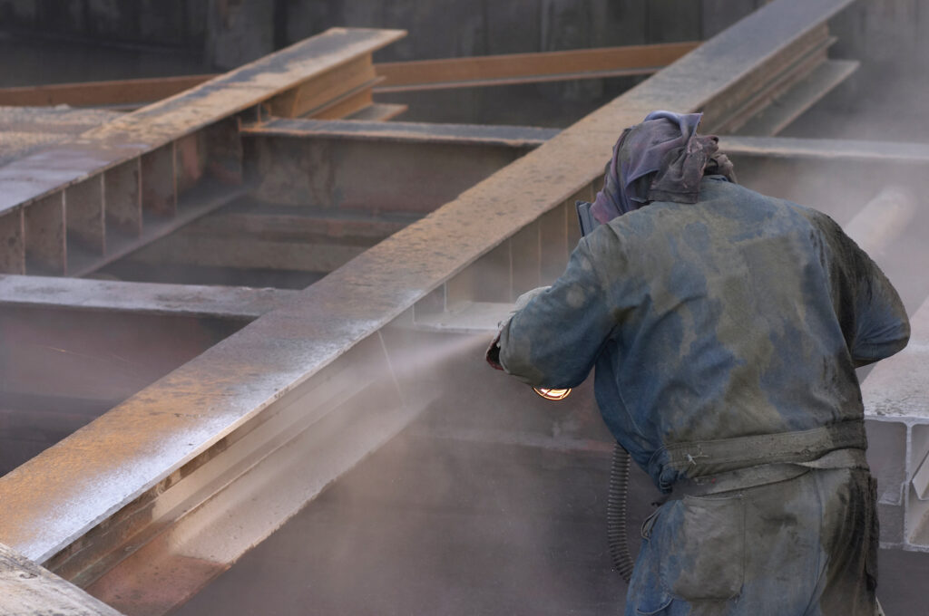Piaskarz czyszczący masywną konstrukcję metalową na zewnątrz – usługi piaskowania Olsztyn